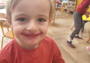 Na zdjęciu widzimy dziewczynkę, która jest uśmiechnięta i ma czerwone "wąsy" po degustacji soku buraczanego.