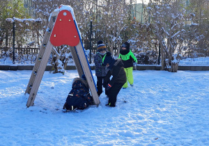Zdjęcie przedstawia dzieci bawiące się na śniegu obok drabinki.