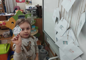 Zdjęcie przedstawia chłopca trzymającego karteczkę z zadaniem adwentowym, wyjęte z kalendarza adwentowego przy którym stoi dziecko.