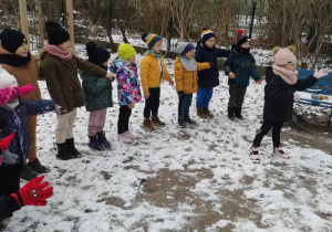 Zdjęcie przedstawia dzieci mówiące rymowankę z pokazywaniem. Dzieci są w ogrodzie przedszkolnym. W ogrodzie jest śnieg.