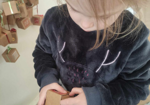 Zdjęcie przedstawia dziewczynkę otwierającą pudełko z kalendarza adwentowego.