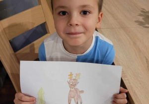 Zdjęcie przedstawia chłopca trzymającego w zdjęciu rysunek renifera.