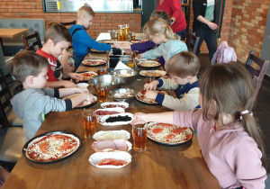 Zdjęcie przedstawia dzieci przy stole przygotowujących pizzę.