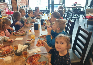 Zdjęcie przedstawia dzieci jedzących pizzę.
