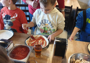 Zdjęcie przedstawia chłopca nakładającego sos na pizzę.