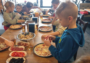 Zdjęcie przedstawia dzieci, które nakładają skłądniki na pizzę.