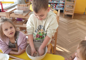 Zdjęcie przedstawia dzieci obserwujące jak chłopiec ugniata ciasto na pierniki.
