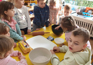 Zdjęcie przedstawia dzieci siedzące przy stole na którym są skłądniki potrzebne do wykonania ciasta na pierniki.