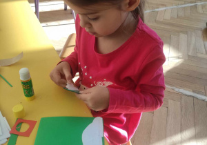 Zdjęcie przedstawia dziewczynkę wykonującą kartkę świąteczną.