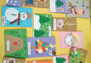 Zdjęcie przedstawia kartki świąteczne wykonane przez dzieci. Kartki leżą rozłożone na stole.