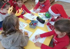Dzieci siedzą przy stoliku i kolorują sylwety Mikołaja.