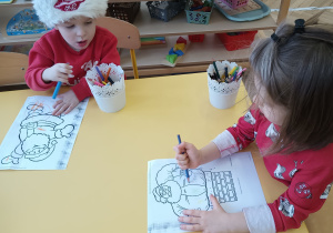 Dzieci siedzą przy stoliku i kolorują sylwety Mikołaja.