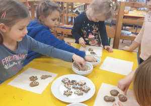 Zdjęcie przedstawia dzieci dekorujące pierniki i układające na talerzu już gotowe ciasteczka.