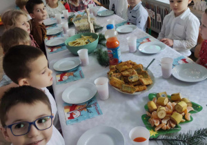 Dzieci siedzą przy stole jedząc potrawy Wigilijne
