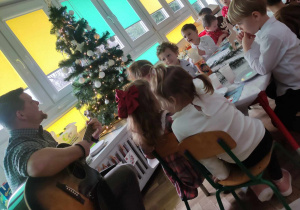 Dzieci słuchają podczas spotkania kolęd granych przez nauczyciela