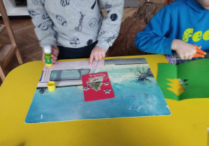 Na zdjęciu widzimy chłopca, który przykleja elementy świąteczne na kartkę. Drugi chłopiec wycina choinkę na swoją kartkę.