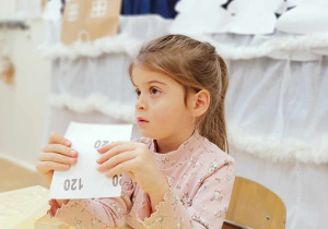 Zdjęcie przedstawia dziewczynkę siedzącą przy stole i słuchającą polecenia. Dziewczynka trzyma w dłoniach papier ścierny.