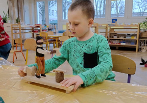Zdjęcie przedstawia chłopca siedzącego przy stole. Chłopiec bawi się drewnianą zabawką.