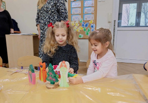 Zdjęcie przedstawia dwie dziewczynki siedzące przy stole. Dziewczynki bawią się drewnianymi zabawkami.