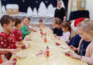 Zdjęcie przedstawia dzieci siedzące przy stole. Dzieci wykonują zabawki z drewna.