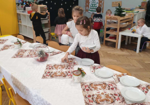 Na zdjęciu widzimy dziewczynki, które rozkładają na stole wigilijnym talerze.