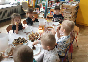 Na zdjęciu widzimy grupkę dzieci, które jedzą słodkości przygotowane przez rodziców.