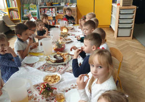Na zdjęciu widzimy grupkę dzieci, które jedzą słodkości przygotowane przez rodziców.