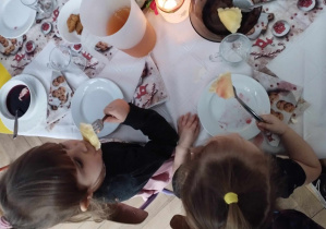 Na zdjęciu widzimy dwie dziewczynki, które jedzą potrawy z wigilijnego stołu.