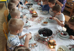 Na zdjęciu widzimy grupkę dzieci, które jedzą barszcz czerwony.