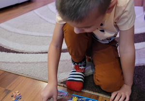 Zdjęcia przedstawia chłopca układającego puzzle na podłodze.