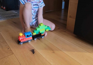 Zdjęcie przedstawia chłopca z zabawką- pociągiem, który wiezie choinkę zbudowaną z klocków.