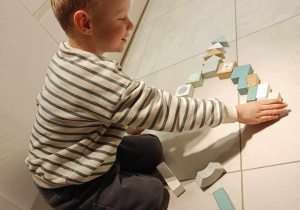 Zdjęcie przedstawia chłopca, który układa na podłodze klocki w kształt choinki.