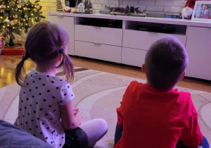 Zdjęcie przedstawia dzieci oglądające bożonarodzeniową bajkę.