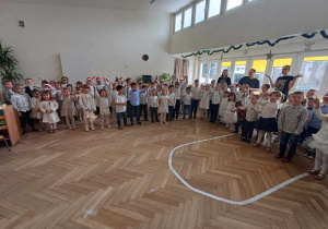 Zdjęcie przedstawia dzieci i nauczycielu stojących w półkolu, śpiewających kolędę.