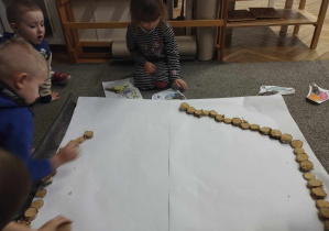 Na zdjęciu widzimy chłopca, który układa ściany karmnika z wykorzystaniem pociętych na krążki drewienek.