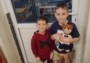Zdjęcie przedstawia dwóch chłopców stojących przy drzwiach. Jeden z chłopców trzyma w rękach Misia Uszatka a drugi torbę papierową.