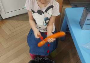 Na zdjęciu widać dziewczynkę, która za pomocą noża obiera marchewkę ze skorki