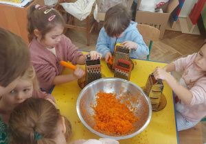 Zdjęcie przedstawia dzieci trące marchewkę na ciasto