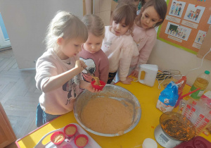 zdjęcie przedstawia dzieci, które nakładają cisto do foremek w kształcie babeczki