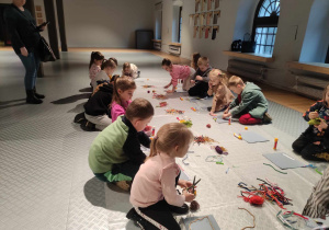 Zdjęcie przedstawia dzieci, które siedzą na podłodze oraz wykonują kompozycje z różnorodnych materiałów.