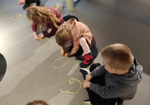 Zdjęcie przedstawia dzieci układające w ustalony kształt żółte sznurki.