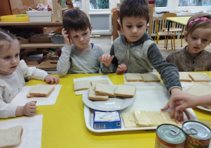 Na zdjęciu widzimy chłopca, który sięga po ser, aby położyć go na kanapki tostowe.