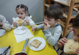 Na zdjęciu widzimy chłopca, który degustuje fasolki w pomidorach. Dziewczynka siedząca koło chłopca zjada swojego tosta.