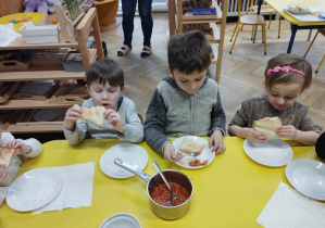 Na zdjęciu widzimy trójkę dzieci, które jedzą tosty.
