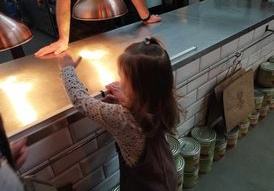 Na zdjęciu widzimy dziewczynkę, która naciska na dzwonek informujący, że danie jest już gotowe.