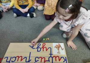 Na zdjęciu widzimy dziewczynkę, która układa napis "Tygrysek" z wykorzystaniem ruchomego alfabetu.