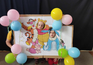 Na zdjęciu widzimy dwójkę dzieci, której robione jest zdjęcie w foto budce z motywem "Kubusia Puchatka".