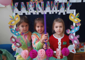 Zdjęcie przedstawia trzy dziewczynki, które pozują do zdjęcia trzymając w rękach ramkę z napisem karnawał. Dziewczynki przebrane są w stroje.