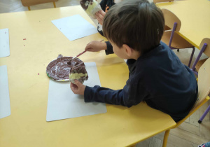 Zdjęcie przedstawia chłopca malującego brązową farbą papierową kulę.