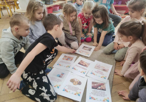 Zdjęcie przedstawia dzieci zgromadzone wokół zdjęć o tematyce tłustego czwartku.